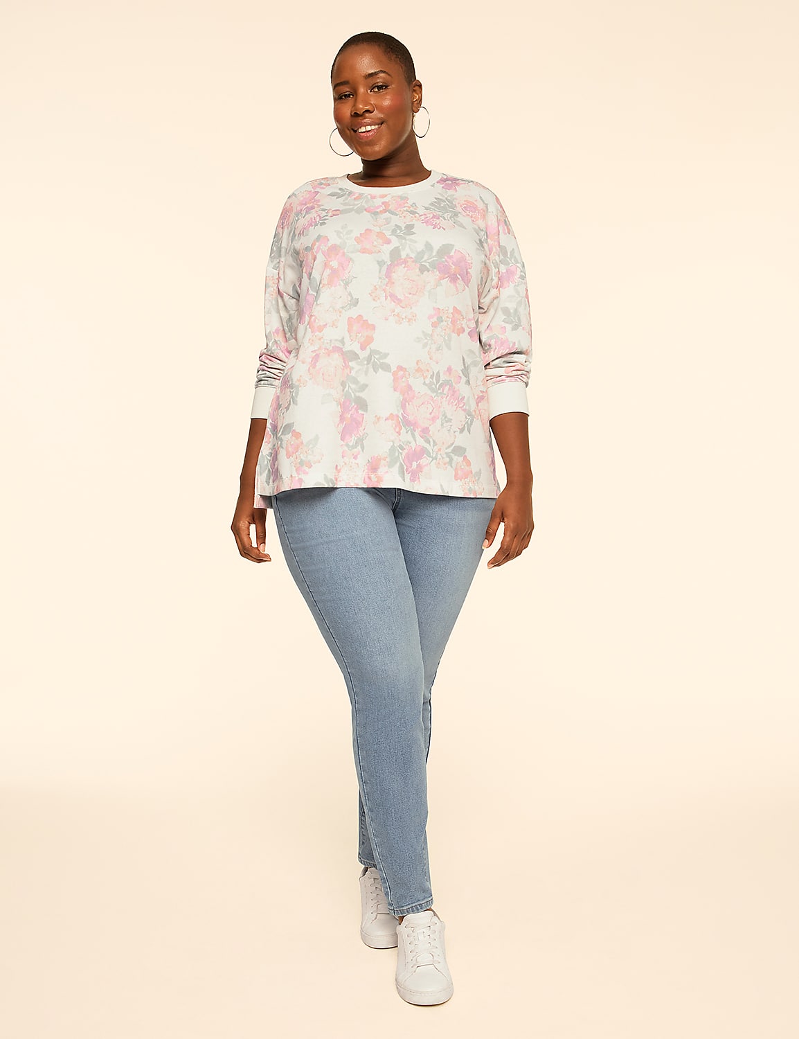 A woman wearing a floral long-sleeved top, blue jeans, and white sneakers stands against a plain, light beige background. Product Image 3