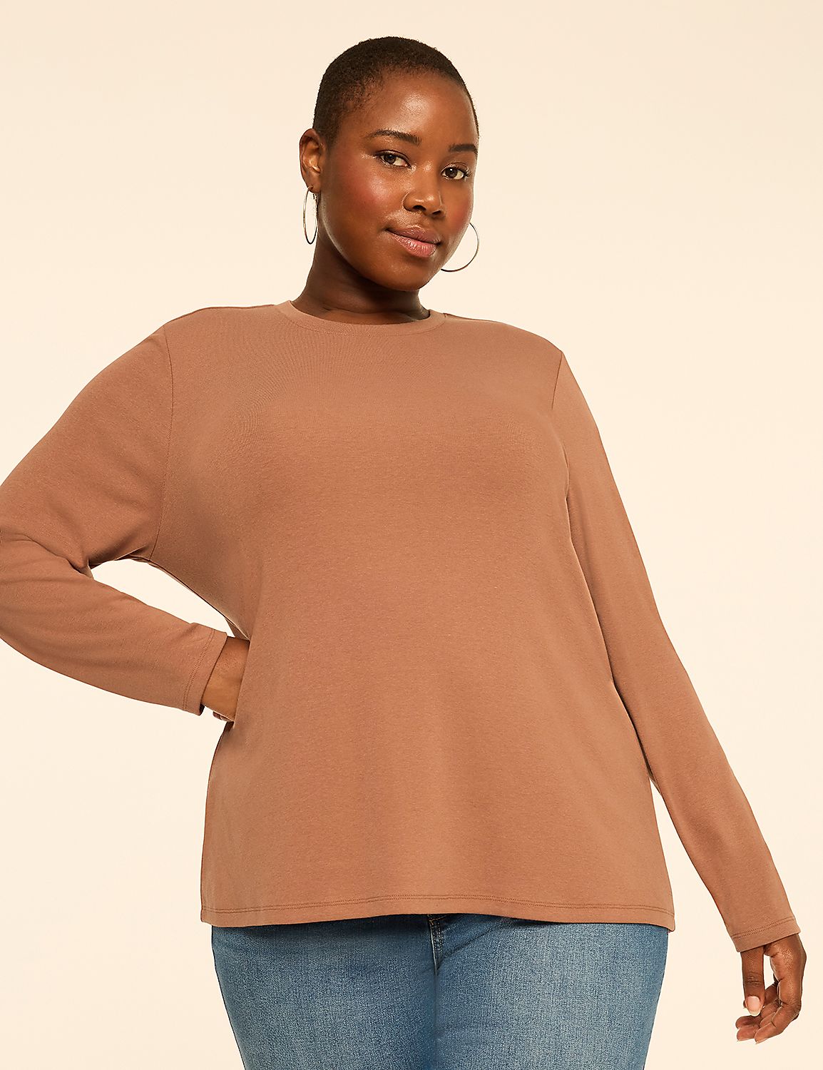 A woman wearing a brown long-sleeved shirt and blue jeans stands against a plain, light-colored background. Product Image 1