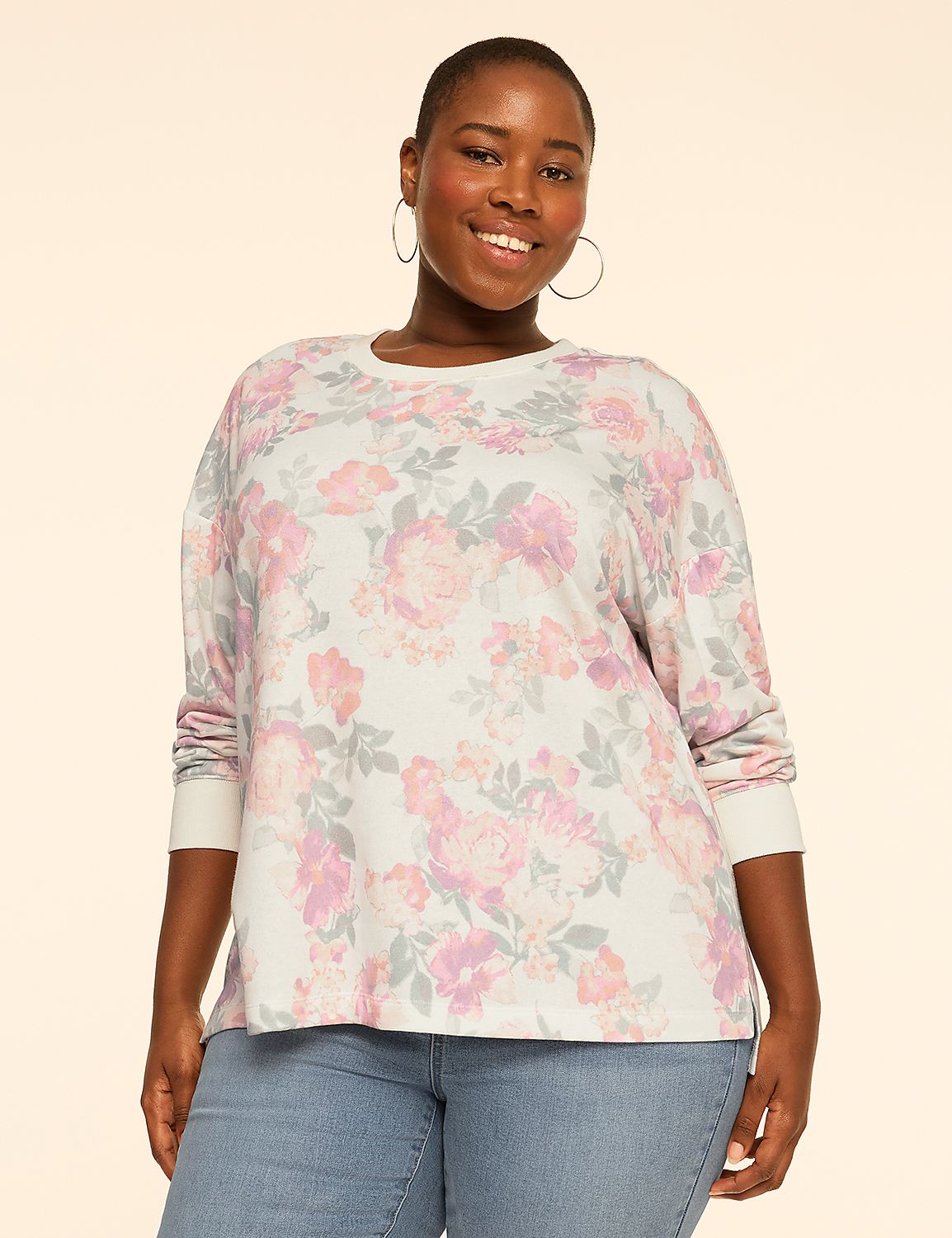 A smiling woman wearing a floral print top and blue jeans stands against a plain, light-colored background. Product Image 1