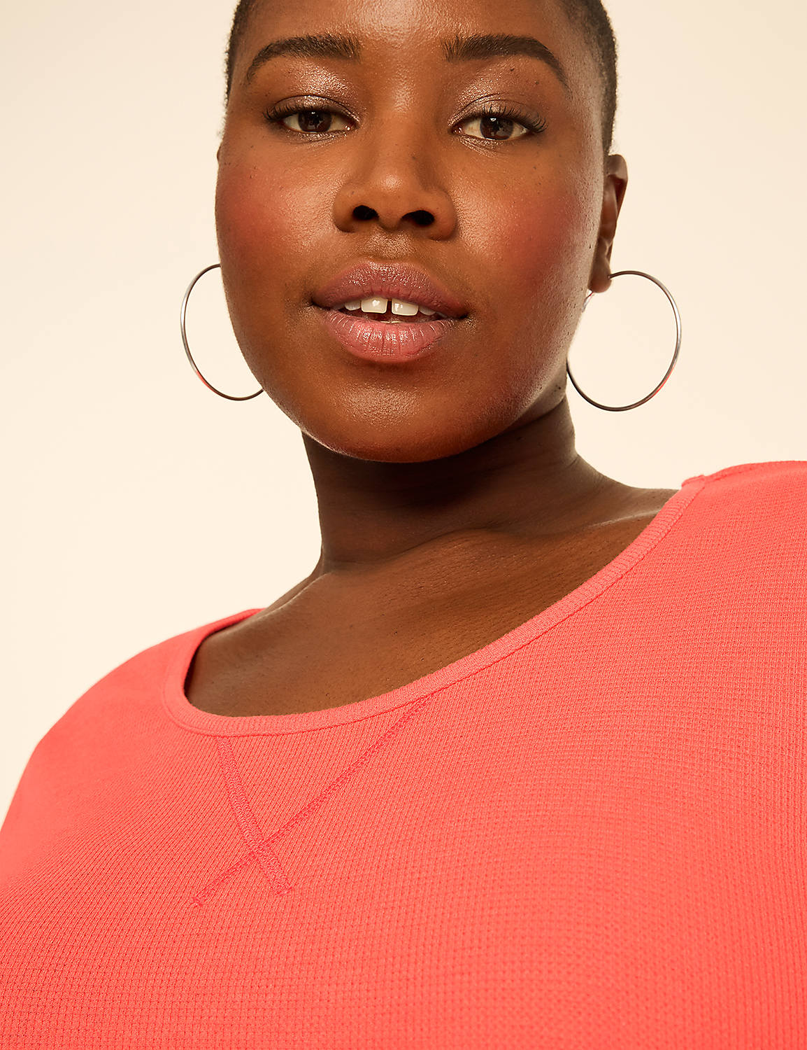 A woman wearing large silver hoop earrings and a coral-colored shirt poses against a plain, light-beige background. Product Image 4
