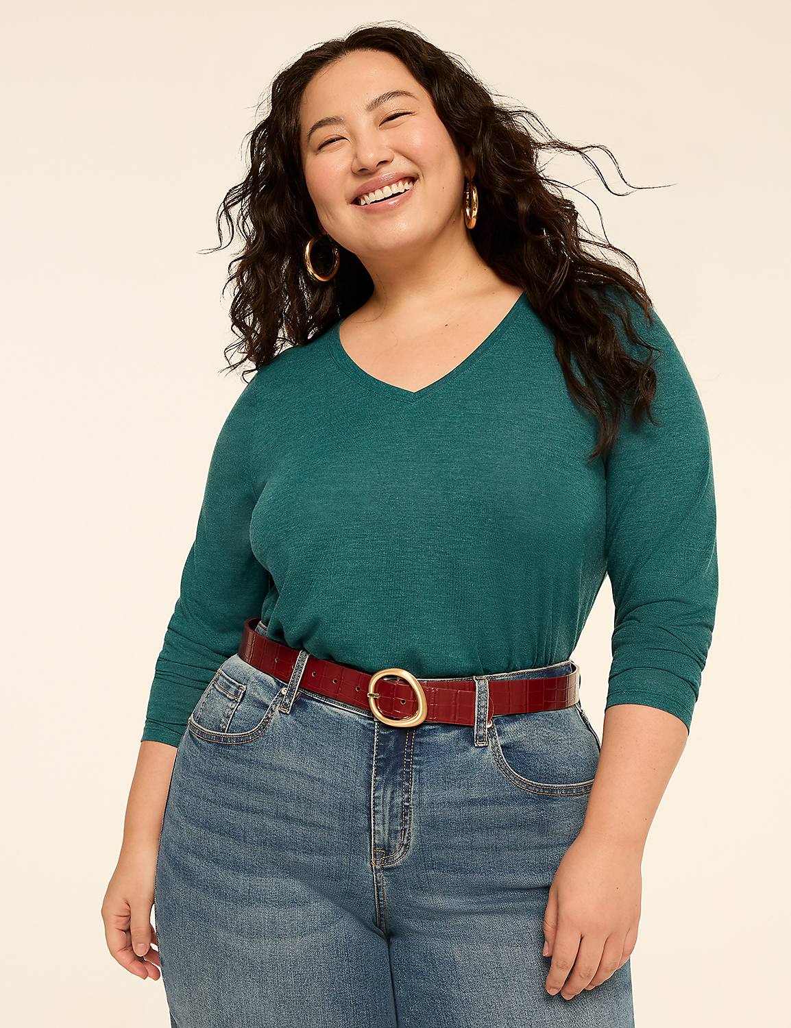 A smiling woman wearing a teal v-neck shirt, red belt, and blue jeans stands against a plain off-white background. Product Image 3