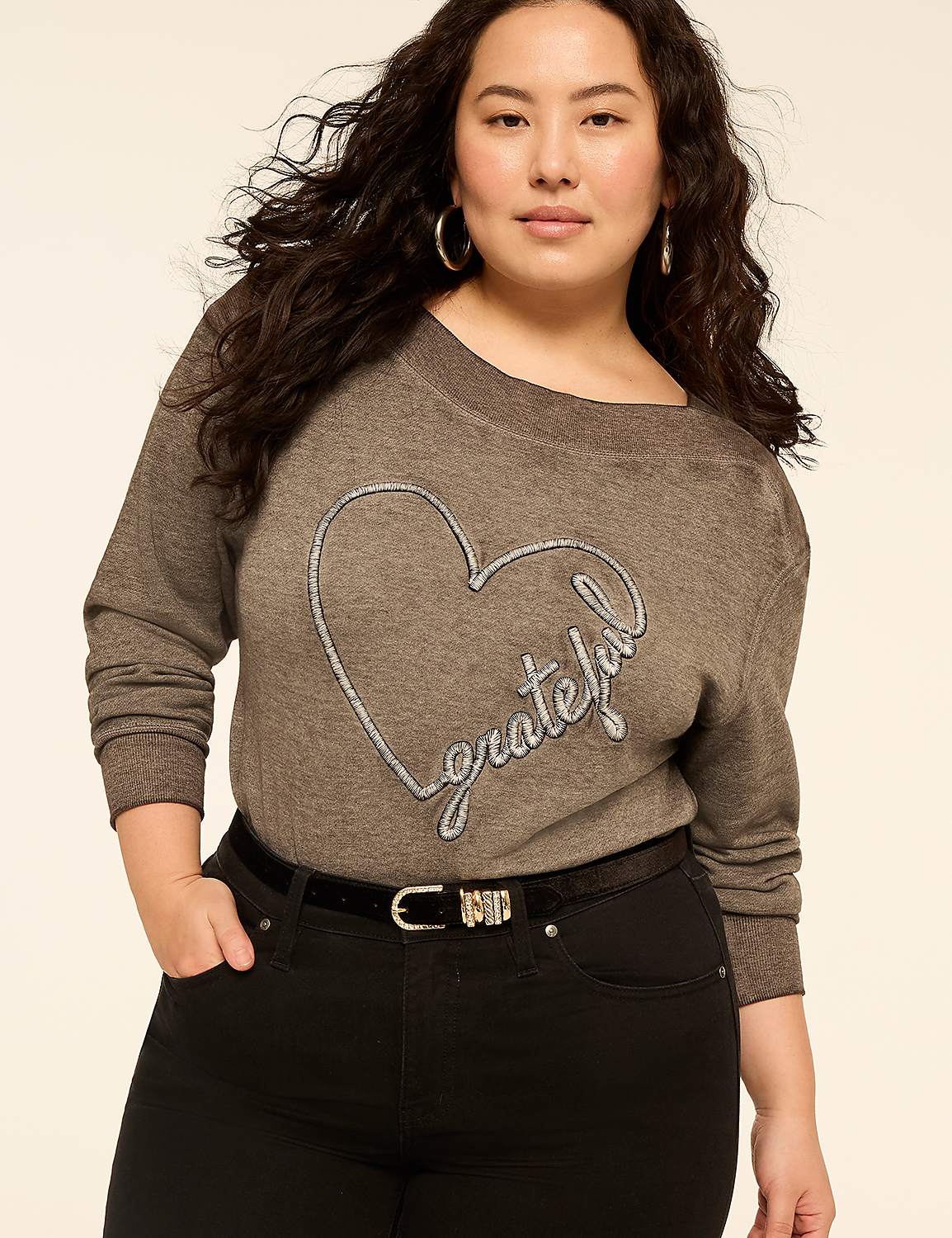A woman wearing a grey sweater with a heart design and black pants stands against a plain, light-colored background. Product Image 2