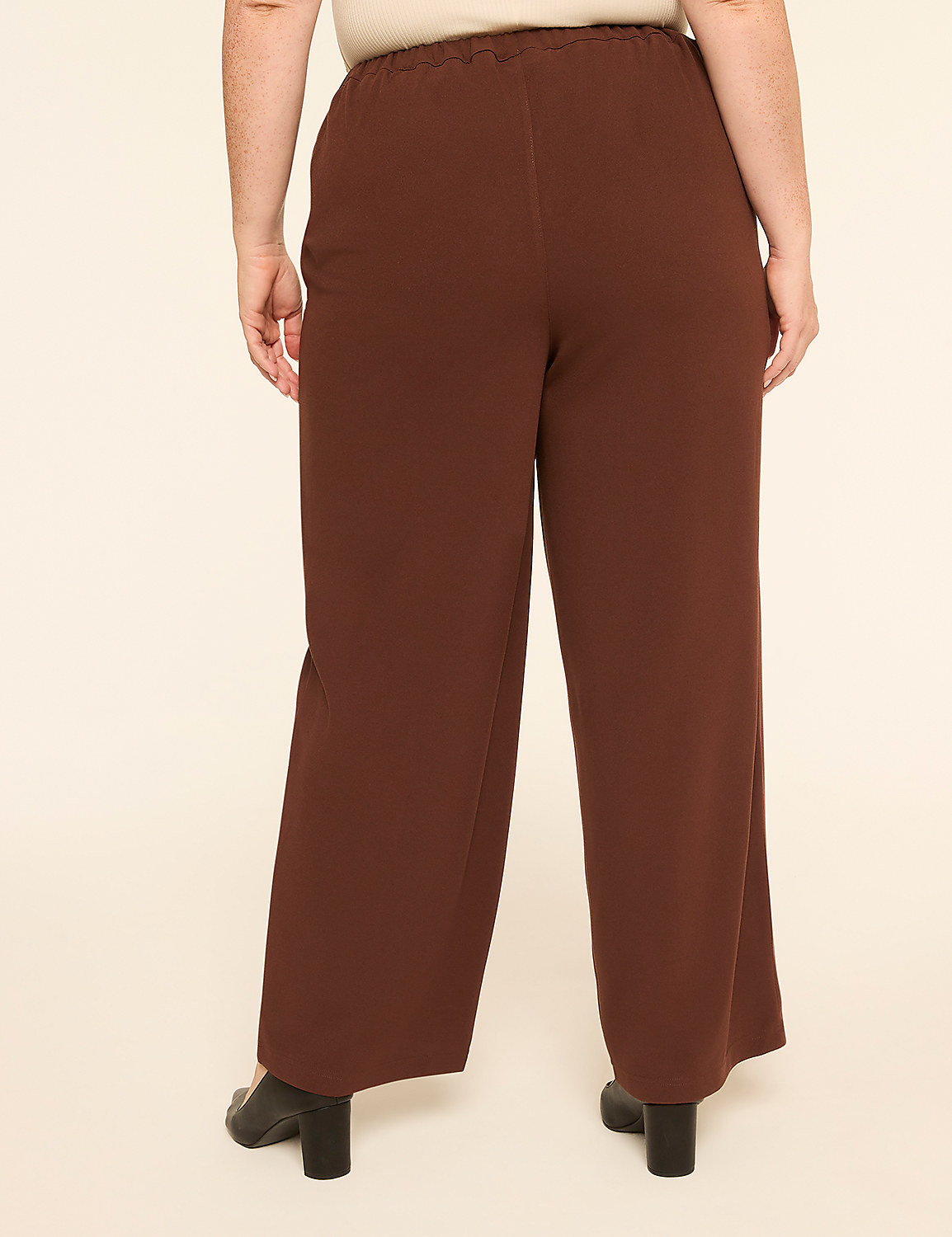 A person stands with their back to the camera wearing wide-leg brown trousers and black heels against a plain, light-colored background. Product Image 2