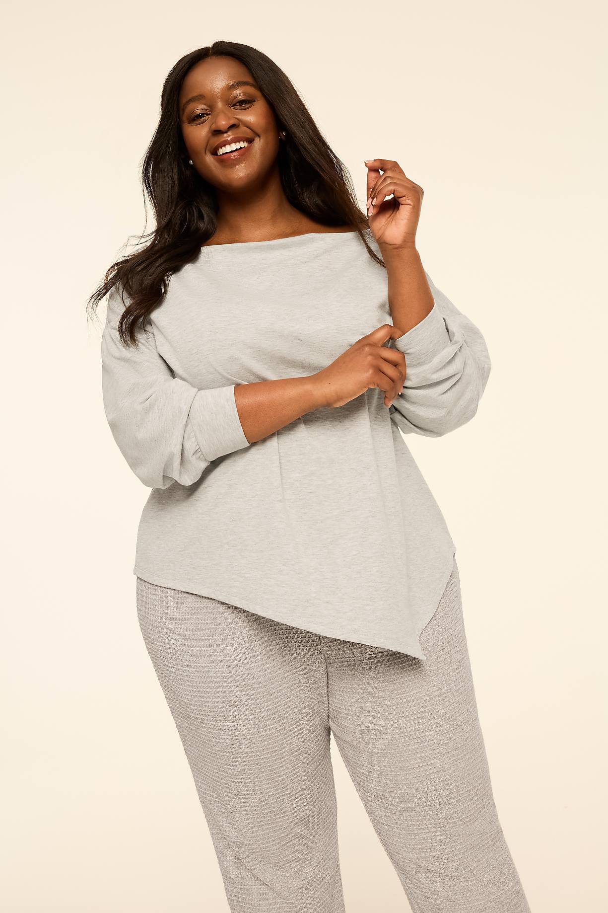 A smiling woman wearing a light grey long-sleeved top and matching textured pants stands against a plain, neutral beige background. Product Image 3