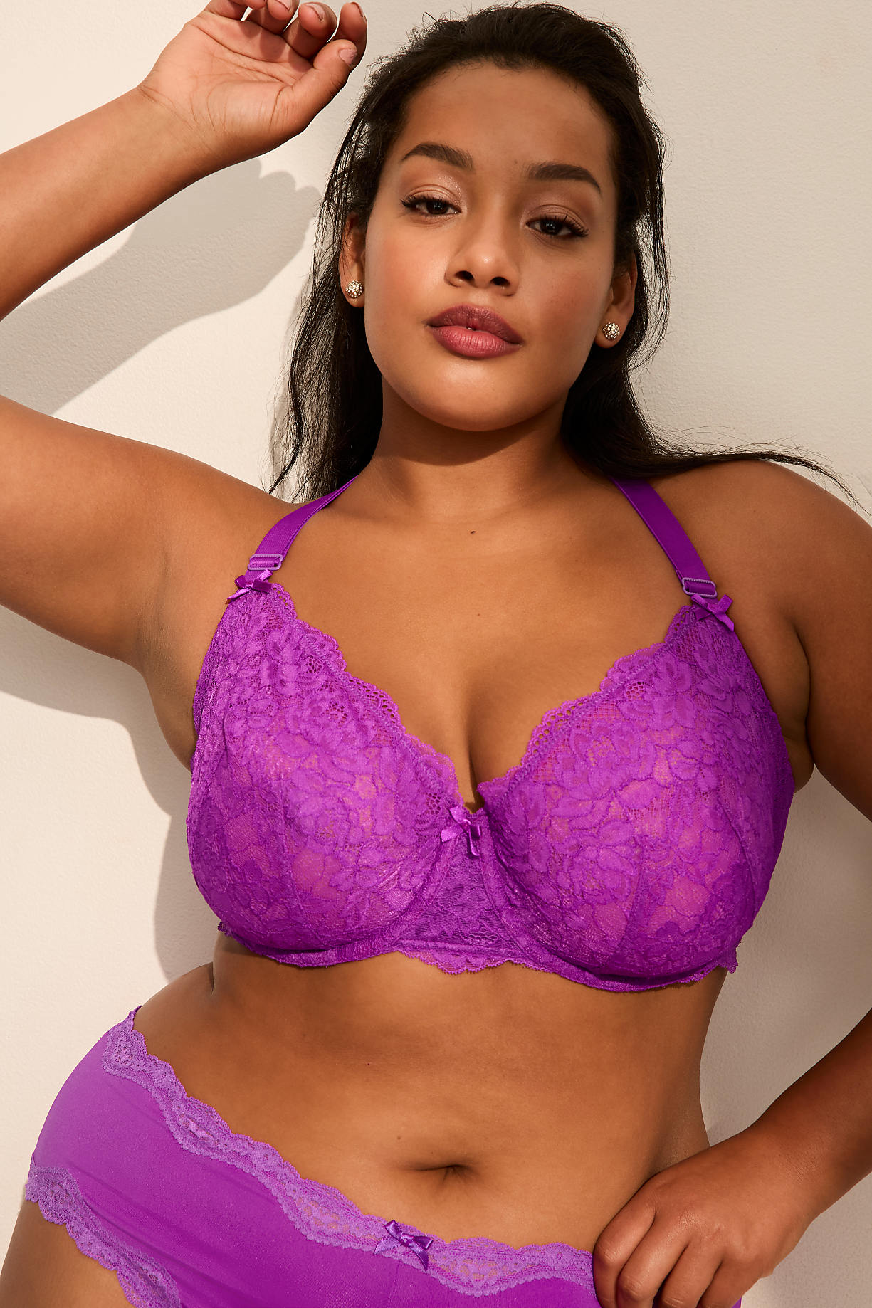 A woman wearing a purple lace lingerie set poses against a plain, light-colored wall. Product Image 11
